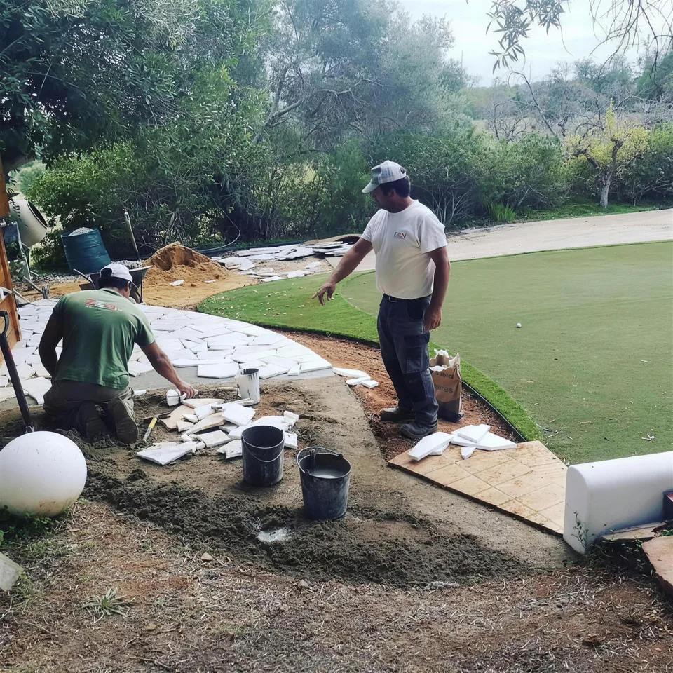 Dois jardineiros a assentar um caminho de lajes junto a um putting green