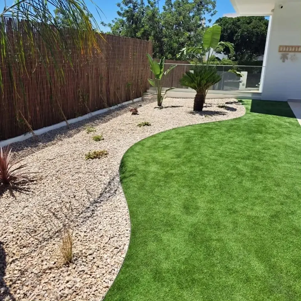 Jardim moderno com relvado sintético curvo, cicas e estrelícias junto a moradia branca
