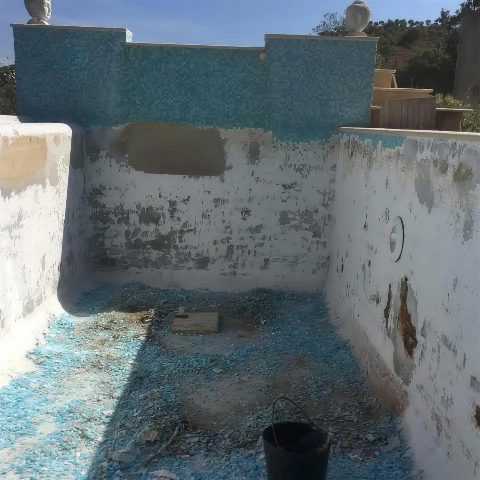 Piscina em obra, com o revestimento removido e cabeças de estátua no muro
