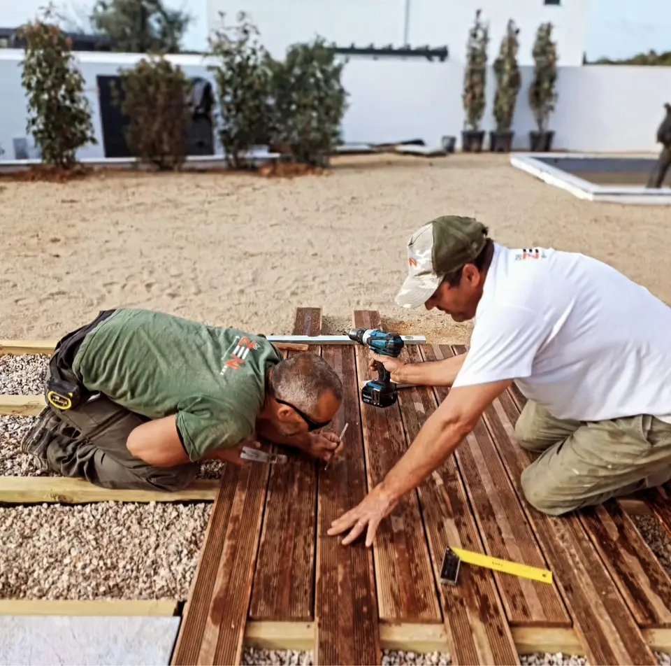Dois jardineiros a fixar um deck de madeira sobre gravilha